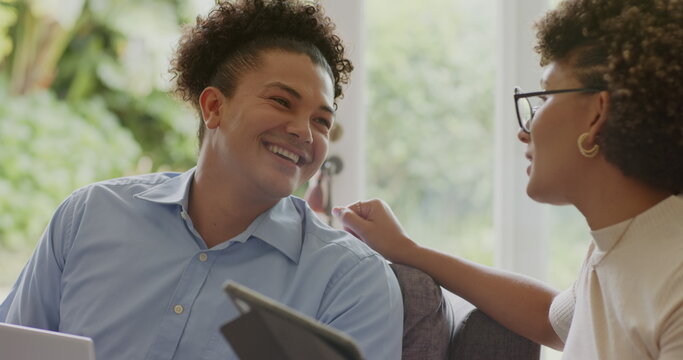 Couple smiling while using tablet and laptop at home, enjoying conversation together