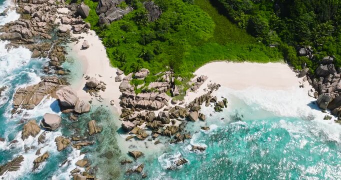 Granite rock formations and lush green foliage line the turquoise waters of the pristine coastline. Seychelles, La Digue. Anse Marron.