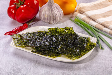 Grey stone surface with dried roasted seaweed sheets on white plate, garlic, red pepper, yellow pepper and green onions, healthy snack © Andrei Starostin