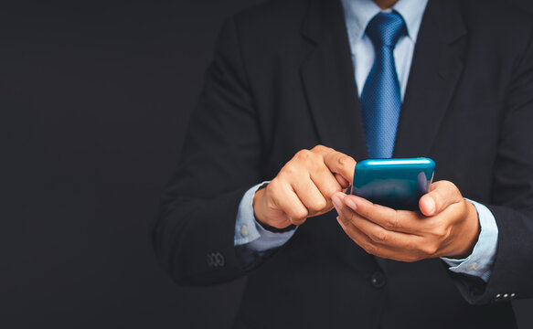 Businessperson in suit using smartphone against dark background  