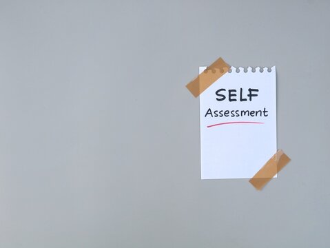 Handwritten self assessment text on a torn notepad paper taped to a grey background. Perfect for business evaluation, personal development, and performance review concept