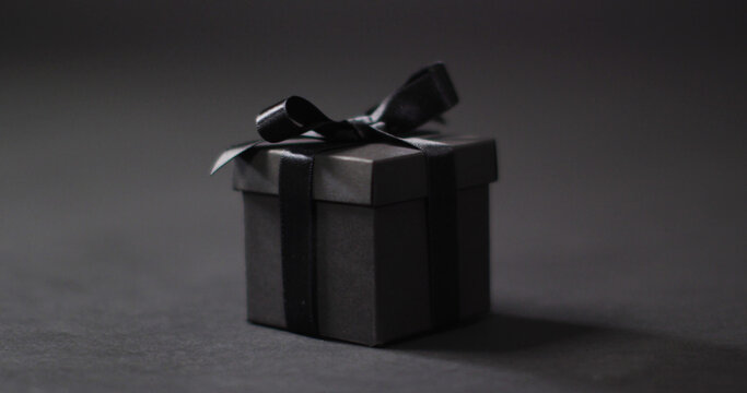 Black gift box with black ribbon on dark grey background with copy space