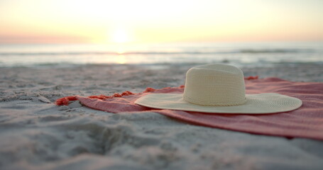A diverse sun hat rests on a beach towel at sunset, with copy space © WavebreakMediaMicro