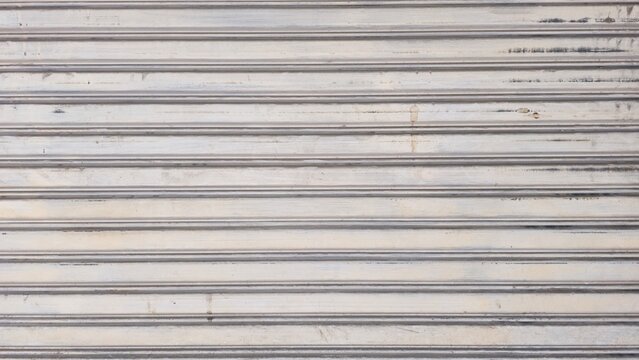 Old dusty metal roller shutter door with stains texture. Grunge rusty metallic rolling gate backdrop background. Abstract horizontal lines pattern on dirty rusty metal door.