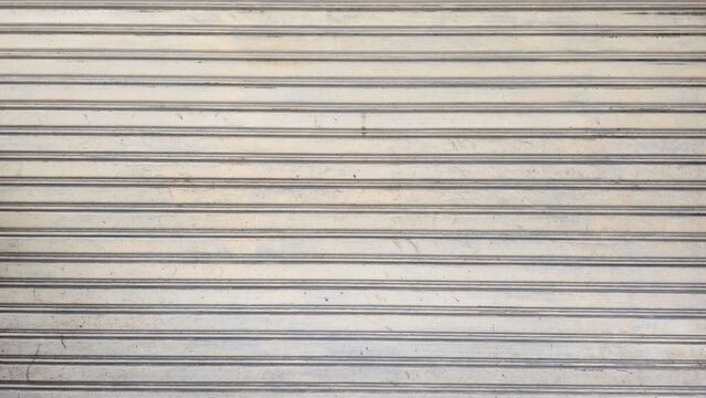 Old dusty metal roller shutter door with stains texture. Grunge rusty metallic rolling gate backdrop background. Abstract horizontal lines pattern on dirty rusty metal door.