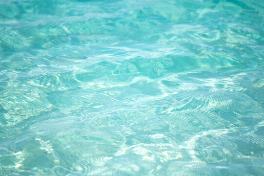 Sparkling turquoise ocean water surface with gentle ripples and bright sun glares reflecting in clear sea during tropical summer day
