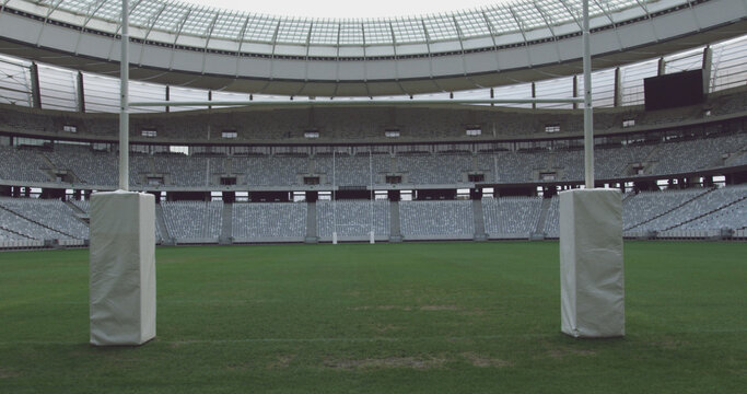 Goal posts on rugby pitch at empty sports stadium with tiered seating, copy space