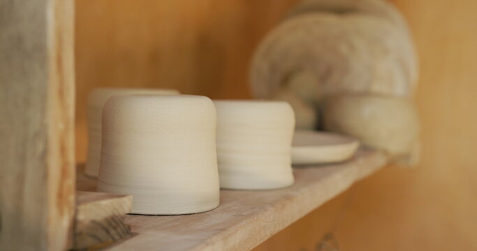 Handmade pots and plates lying on shelf in pottery workshop