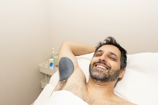 Smiling man undergoing underarm waxing hair removal
