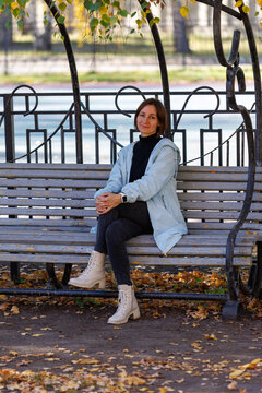 Woman sits on park bench, autumn leaves scattered around