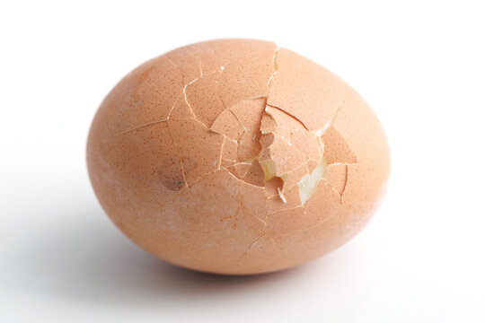 Cracked brown egg rests on plain white background