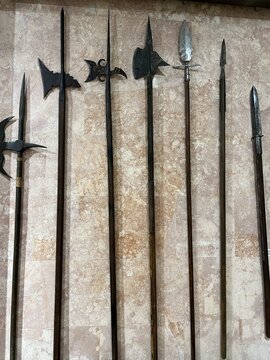 Collection of medieval polearms with iron blades and long wooden shafts displayed in a museum