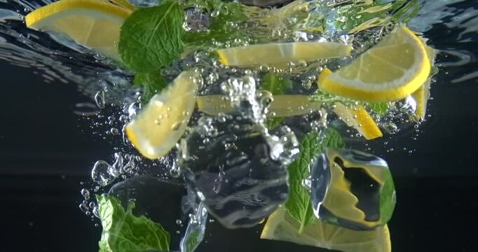 Ice cubes mint leaves and lemon slices falling into water with splash in slow motion