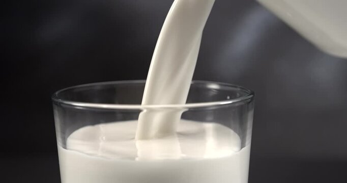 Milk pouring into glass with splash in slow motion close up black background