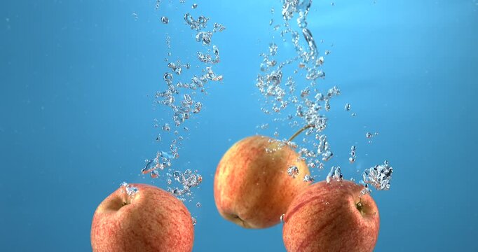 Apples falling into water with splash in slow motion on blue background