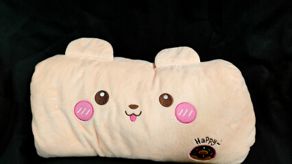Cute peach plush bear pillow with embroidered kawaii face, pink cheeks and chocolate donut on black sofa background, soft cushion toy © Ekarin