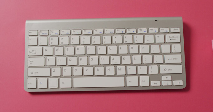 Overhead view of computer keyboard, shopping trolley on pink background
