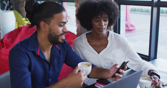 Diverse couple sitting at a table in a cafe drinking coffee using laptop and talking