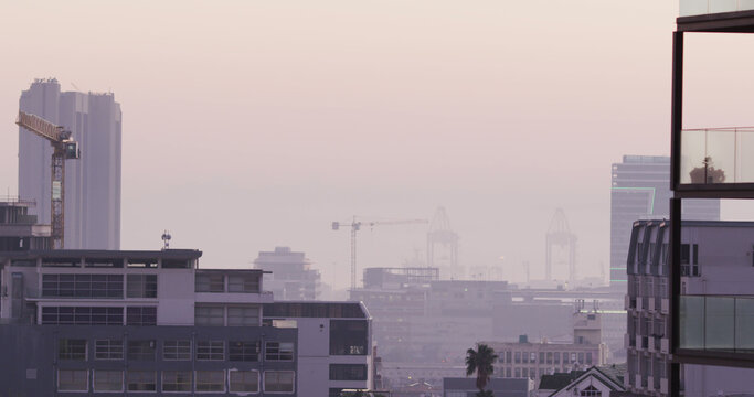 General view of cityscape with multiple buildings, construction site and shipyard covered in fog