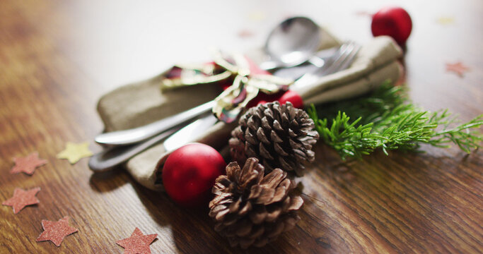 Image of christmas decorations with bauble and pine cones and cutlery on wooden background