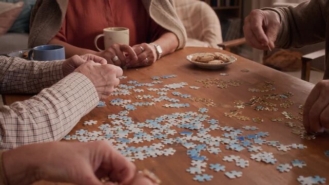 Diverse senior friends assembling jigsaw puzzle together at table while socializing. Footage useful for active aging, retirement community living, and cognitive wellness campaigns