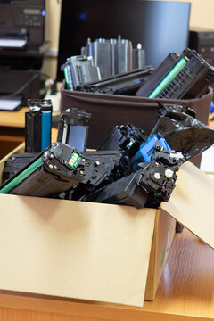 Collection of used printer toner cartridges in a cardboard box prepared for recycling and responsible electronic waste management.