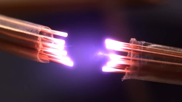 Electric arc sparks between exposed copper cable ends against a dark background