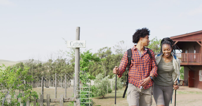 Happy african american couple with backpacks, hiking with trekking poles together, slow motion