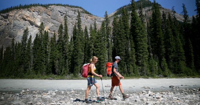Side view of young caucasian hiker couple with backpack hiking near riverside in the forest