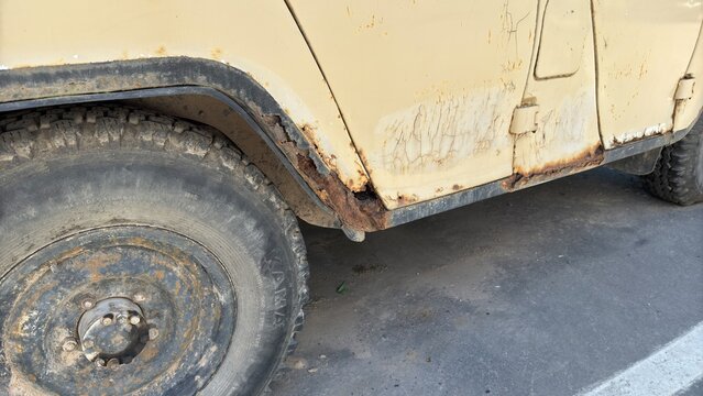 Rust damage around the wheel arch and lower body of an old off road vehicle, revealing advanced metal corrosion and deteriorating automotive paint