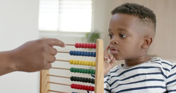 African American dad and child at home, dad pointing red abacus beads, child reaching, learning
