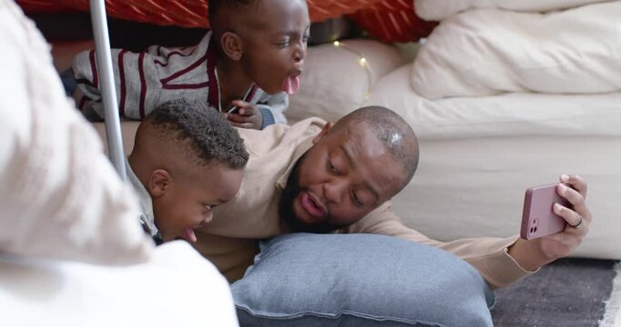 African American father with two sons lifting pink phone, making faces as boys mimicking under fort