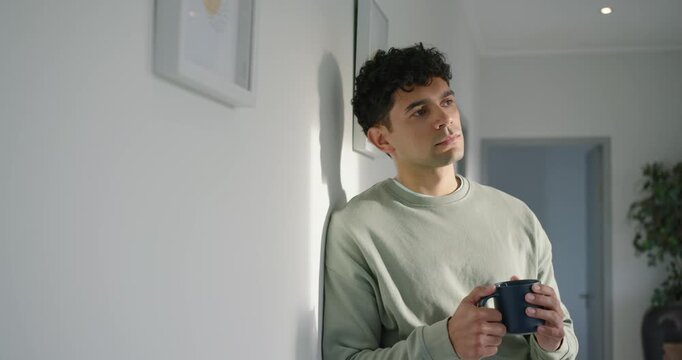 African American man leaning in hallway holding dark mug, sunlight urging gaze shifting, smiling