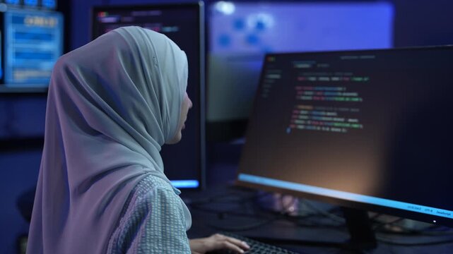 Muslim female software developer in hijab coding on multiple monitors in dark office, Happy programmer working on IT system and software development, Modern technology, cybersecurity and data concept