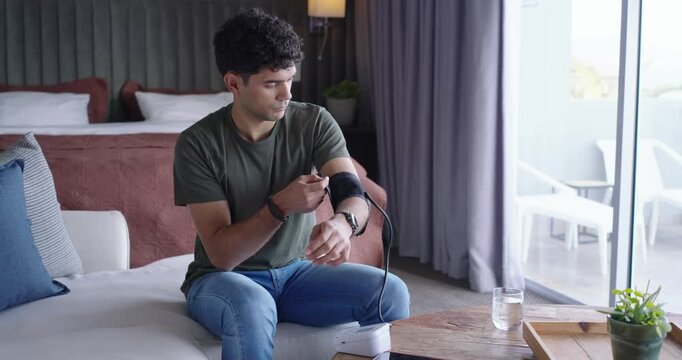 African American man on sofa reaching for black cuff and white monitor, checking blood pressure