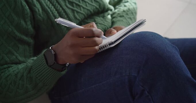 African man pausing tapping pen and journaling capturing ideas in spiral notebook on floor