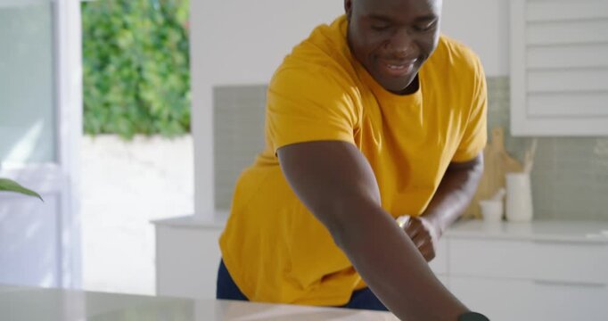 Man in yellow shirt spraying bottle and wiping spill on white island with cloth, inspecting smiling