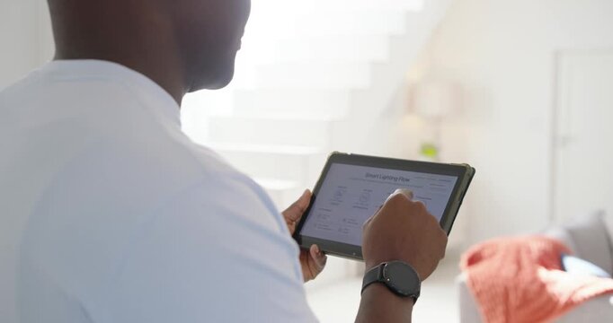 African American man in tee opening light app tapping tablet testing lights in living-room