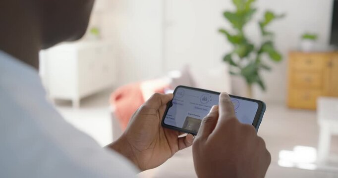 African American man in tee with dark smartwatch responding to prompt, tapping phone in living room