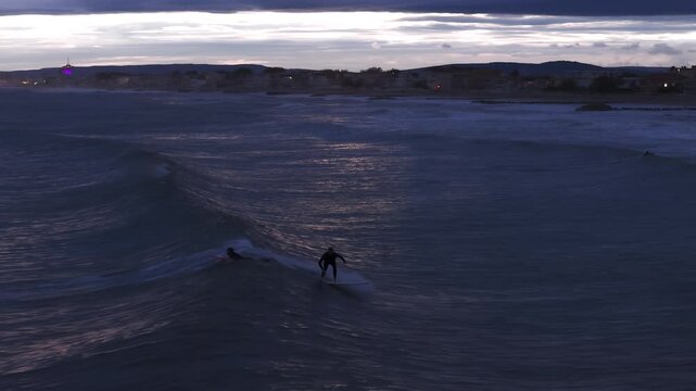 Surfers riding waves near Carnon beach at blue hour