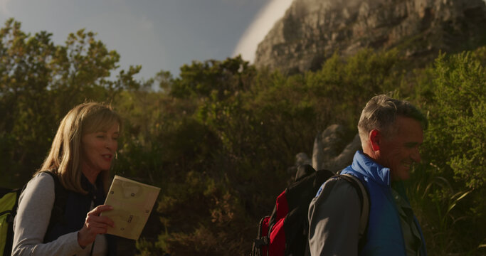 Happy senior caucasian couple hiking in sunny countryside with backpacks and map