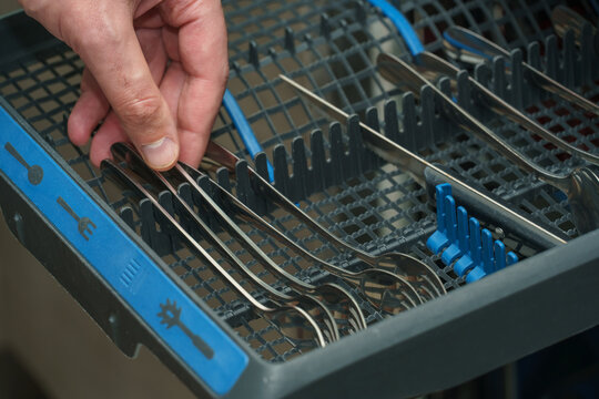 Close-up of a hand placing stainless steel forks into the cutlery compartment of a dishwasher
