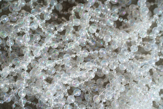 Close-up of translucent decorative bead garlands with an iridescent finish, reflecting subtle pastel colors. Christmas styling, festive crafts, elegant event decoration