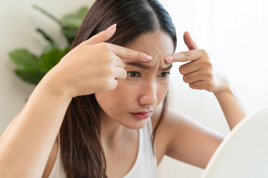 An Asian young woman looking at the mirror and feeling worried about her facial skin problem that cracked and aging.