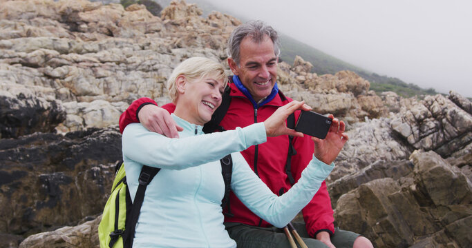Senior couple enjoys a video call during a seaside hiking break.