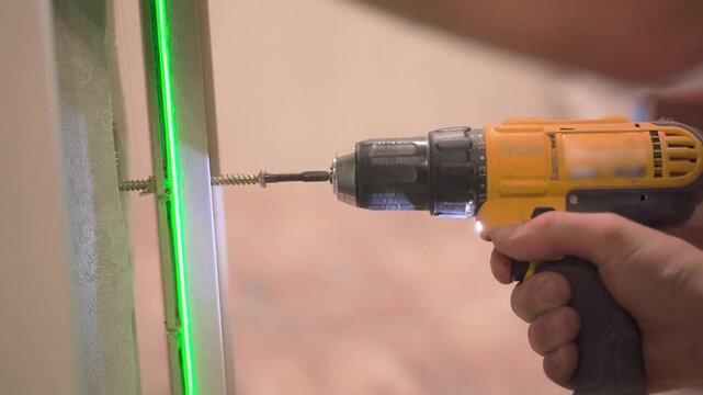 Yellow cordless drill driving long screw into door frame along green laser line
