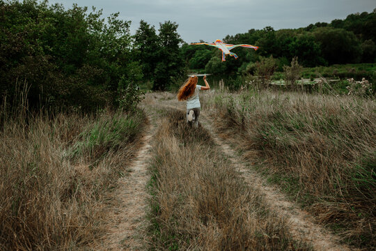 Child running with kite on dirt road among grass