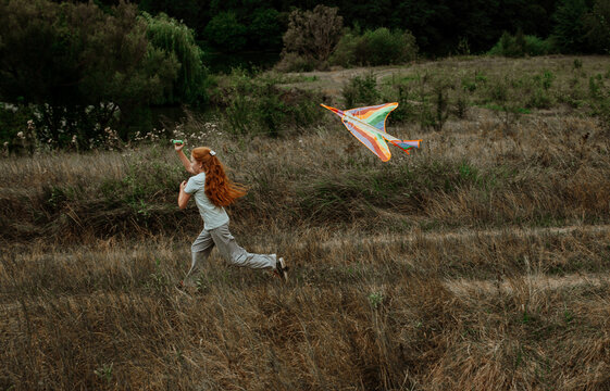 Girl running with kite through summer meadow
