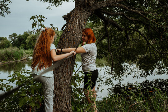 Mother and daughter hanging hammock on tree by lake