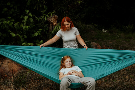 Mother rocking girl in hammock in forest